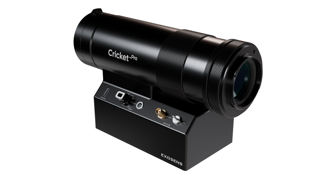 Black, cylindrical Cricket™ Pro imaging device mounted on a compact base, featuring a large front optical lens, textured grip rings, and front-panel controls and connectors; branded “Exosens” on the base, shown against a dark background.