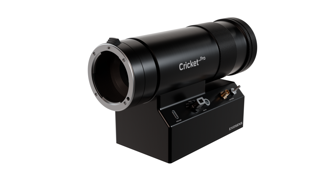 Black, cylindrical Cricket™ Pro imaging device mounted on a compact base, featuring a large front optical lens, textured grip rings, and front-panel controls and connectors; branded “Exosens” on the base, shown against a dark background.