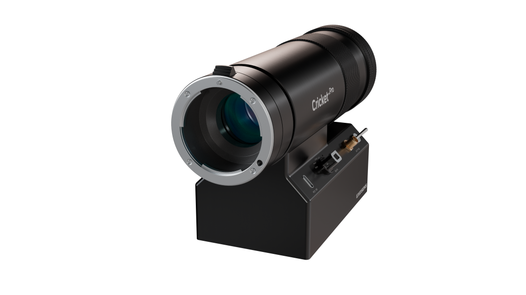Black, cylindrical Cricket™ Pro imaging device mounted on a compact base, featuring a large front optical lens, textured grip rings, and front-panel controls and connectors; branded “Exosens” on the base, shown against a dark background.