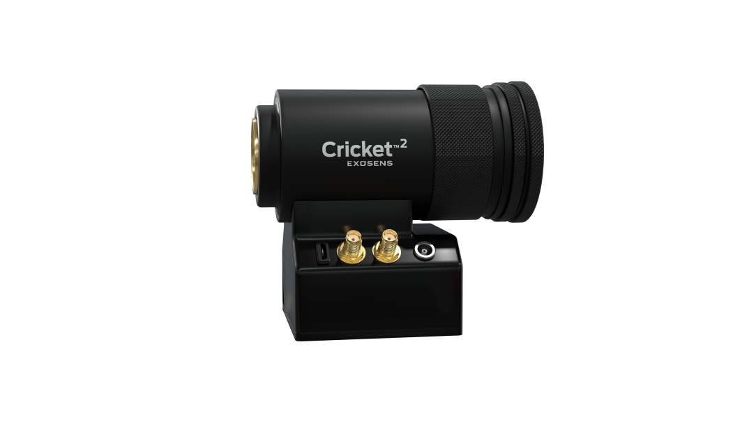 Black, cylindrical Cricket™2 imaging device mounted on a compact base, featuring a large front optical lens, textured grip rings, and front-panel controls and connectors; branded “Exosens” on the base, shown against a white background.